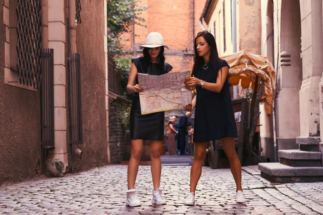 Due turiste che consultano una mappa mentre passeggiano in una strada di una città storica.