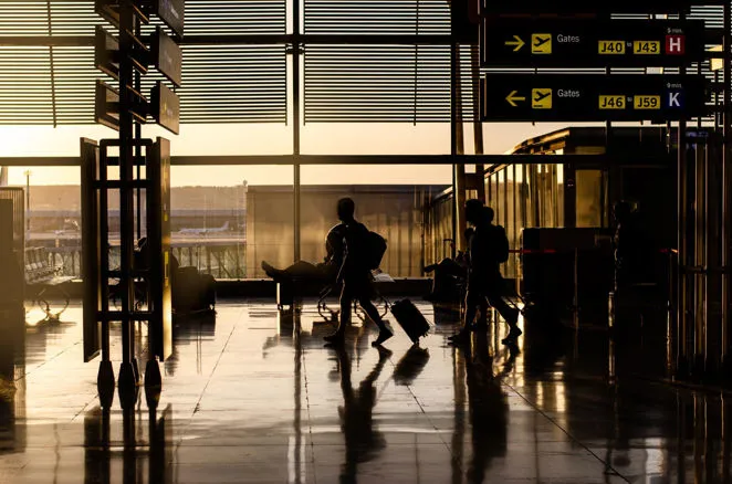 Passeggeri in aeroporto con valigie al tramonto in attesa del servizio transfer.